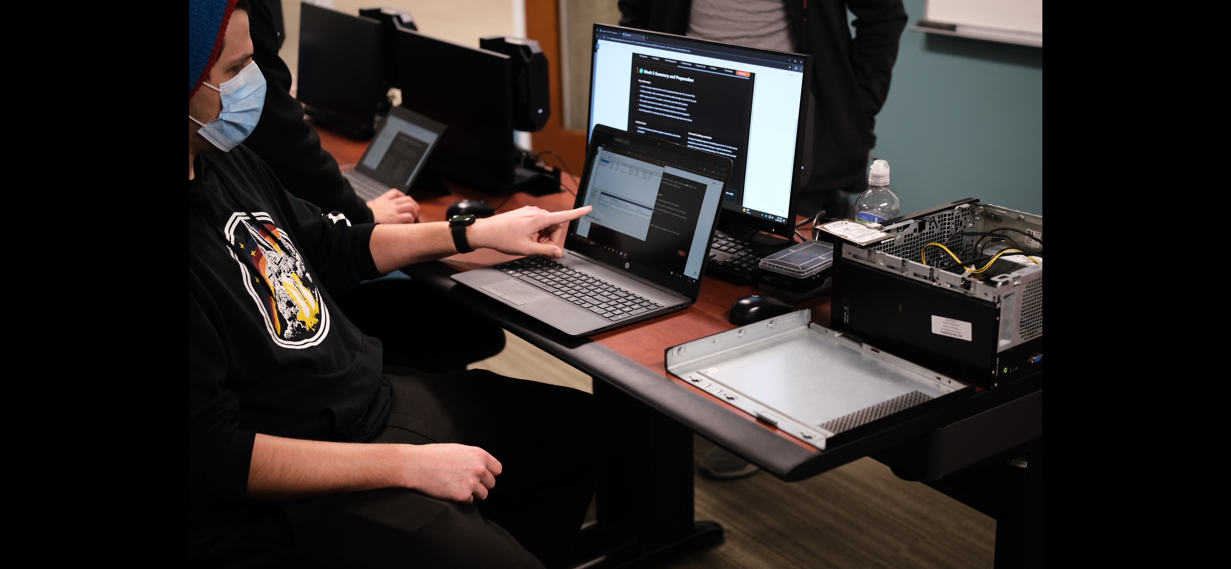 Student pointing at laptop screen with PC parts nearby